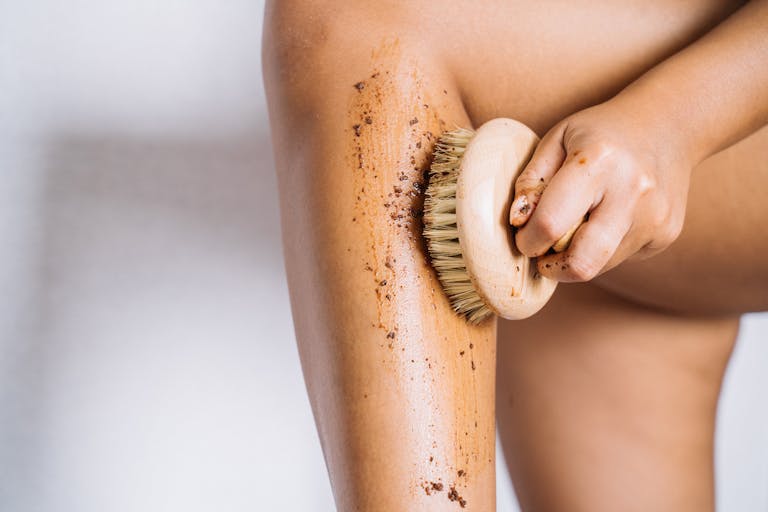 Detailed image of a hand using a brush for exfoliating a leg, showcasing skincare routine.