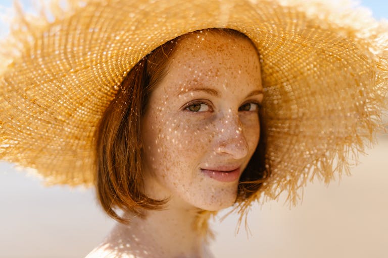 Close-up of a smiling woman with freckles wearing a straw hat outdoors.