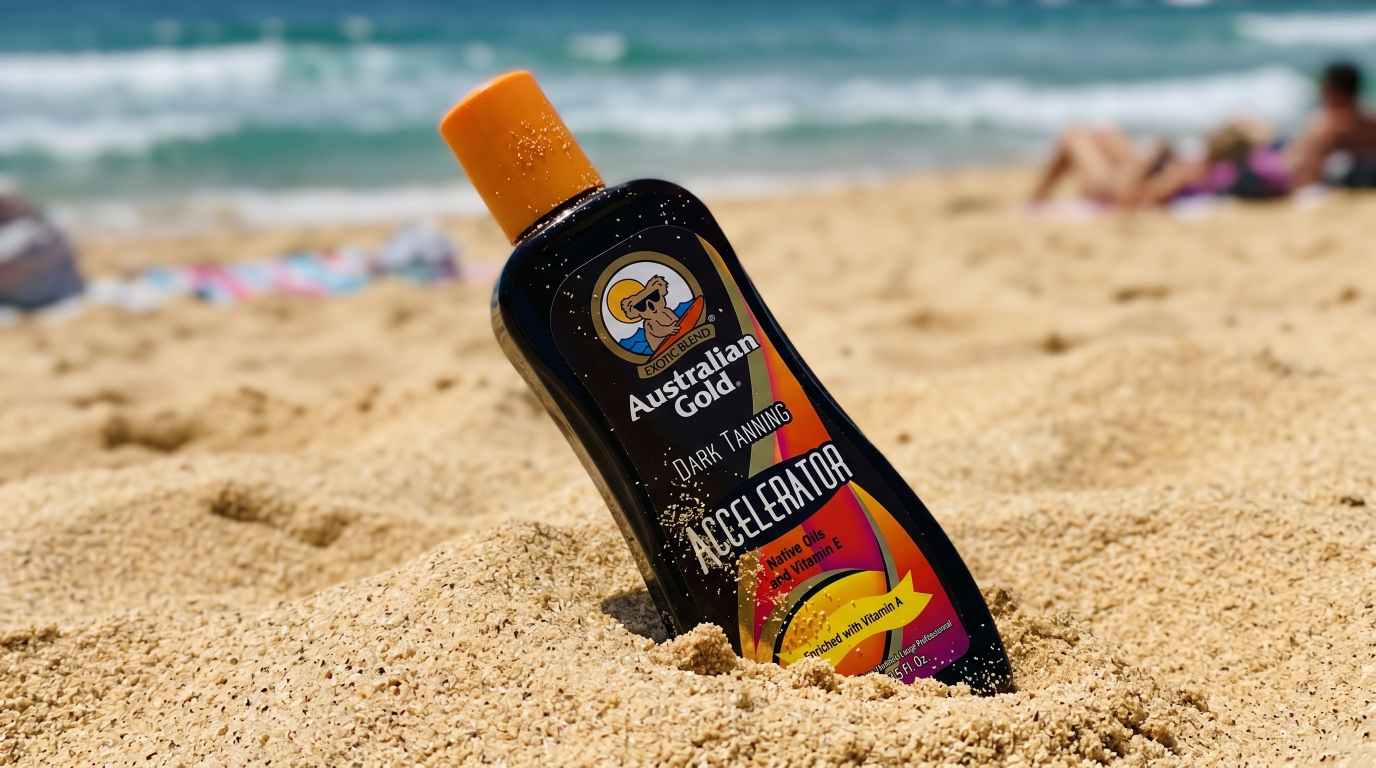 Australian Gold Dark Tanning Accelerator bottle in beach sand with ocean in the background