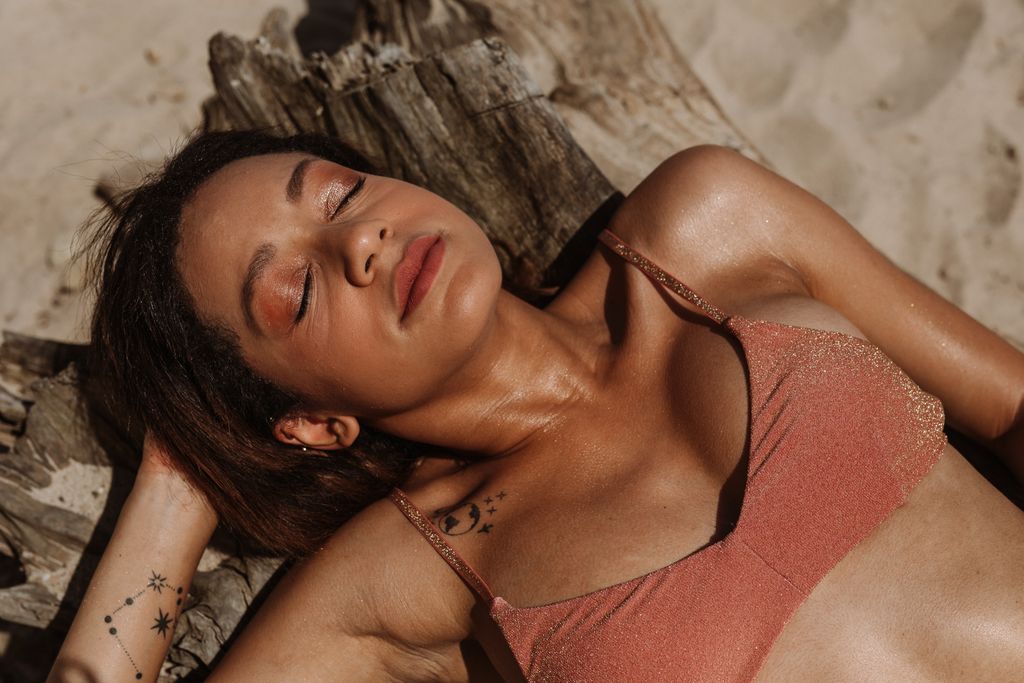A woman enjoys sunbathing on a sandy beach, eyes closed in relaxation, under the warm summer sun.