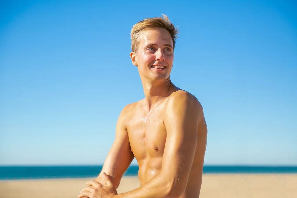 Shirtless man with a bright smile enjoying a sunny day at the beach.